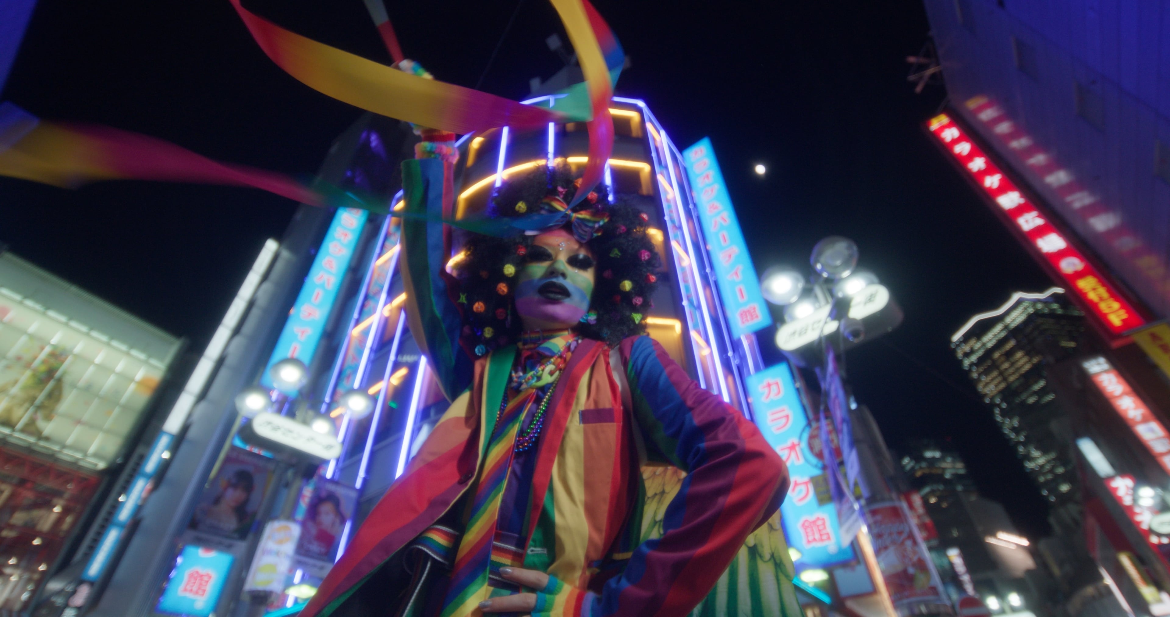 Decora performer in a rainbow costume before a wall of Tokyo neon at night, plain Rec.709 conversion