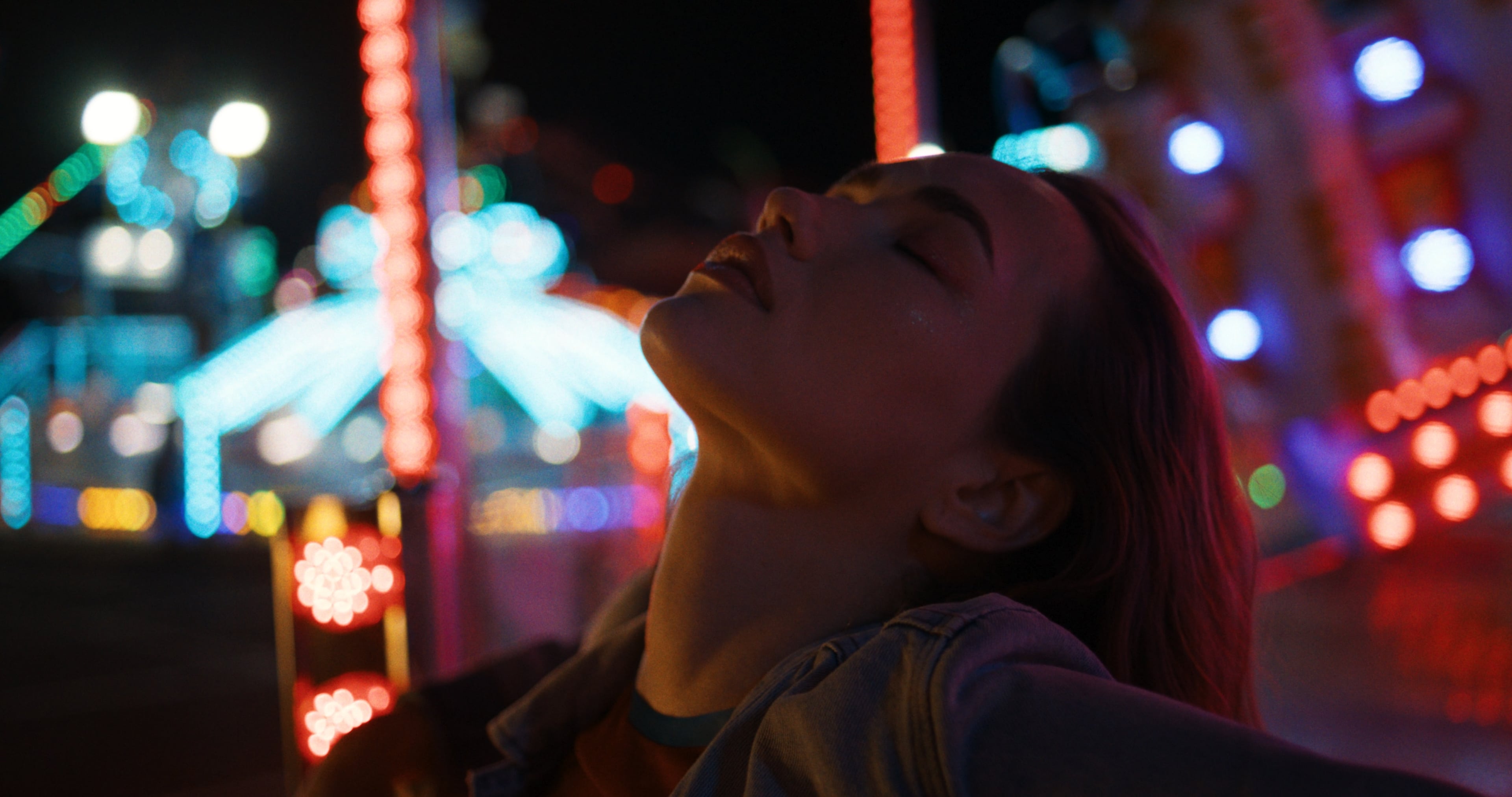 Woman lit by red rim light at a night funfair, carousel bokeh behind, rendered through Latent