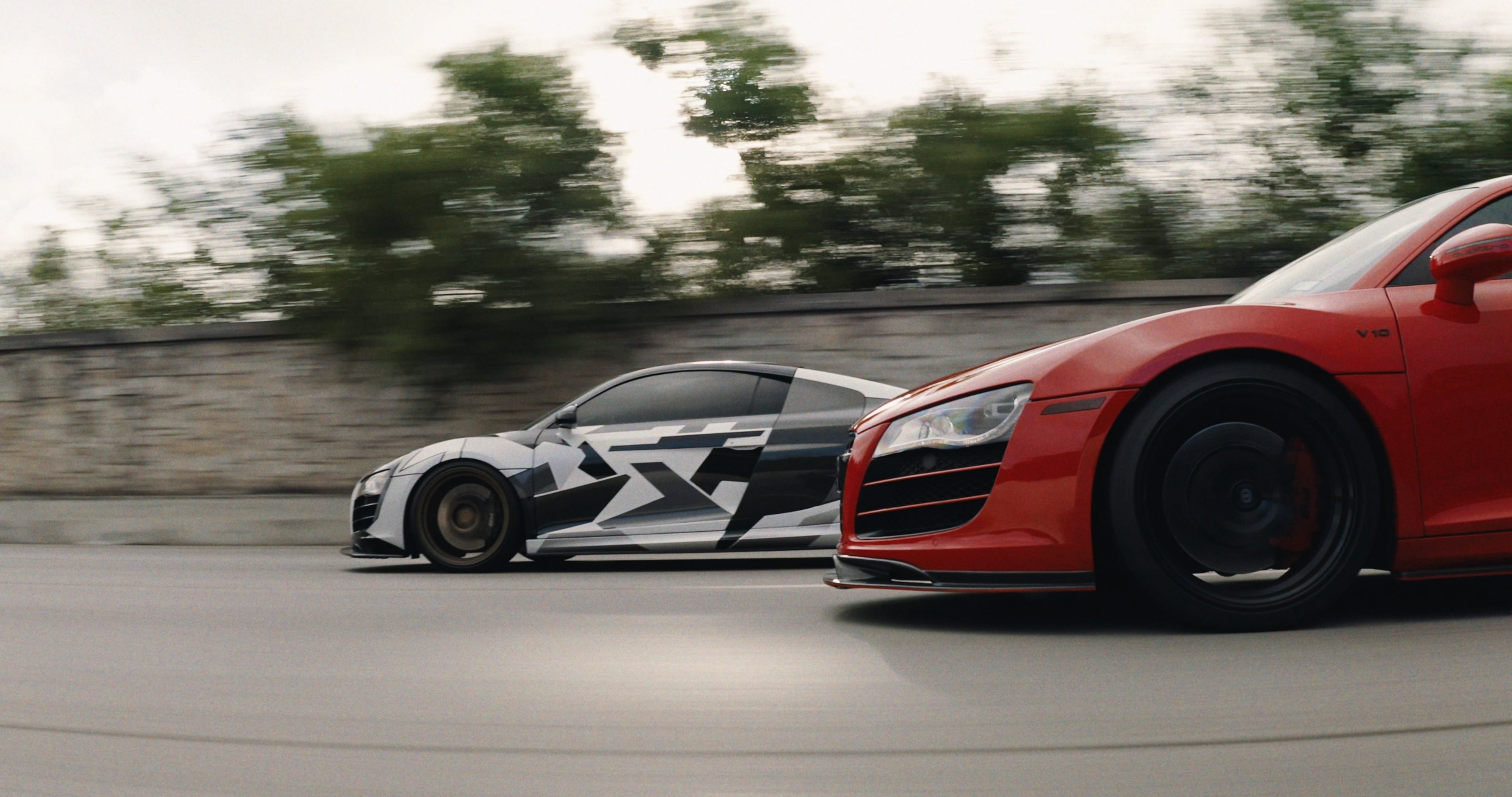 Red Audi R8 racing past a stone wall under an overcast sky, rendered through Latent